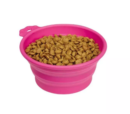 Pink collapsible bowl filled with dog food on a white background