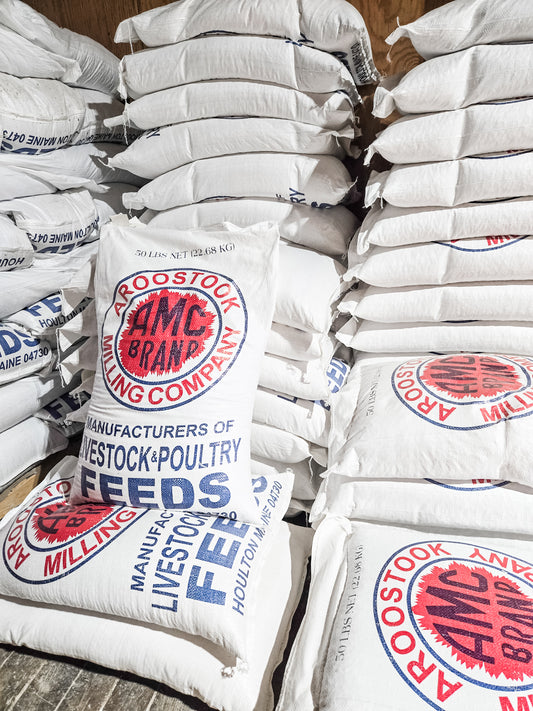 Stack of AMC Brand feed bags on a wooden floor