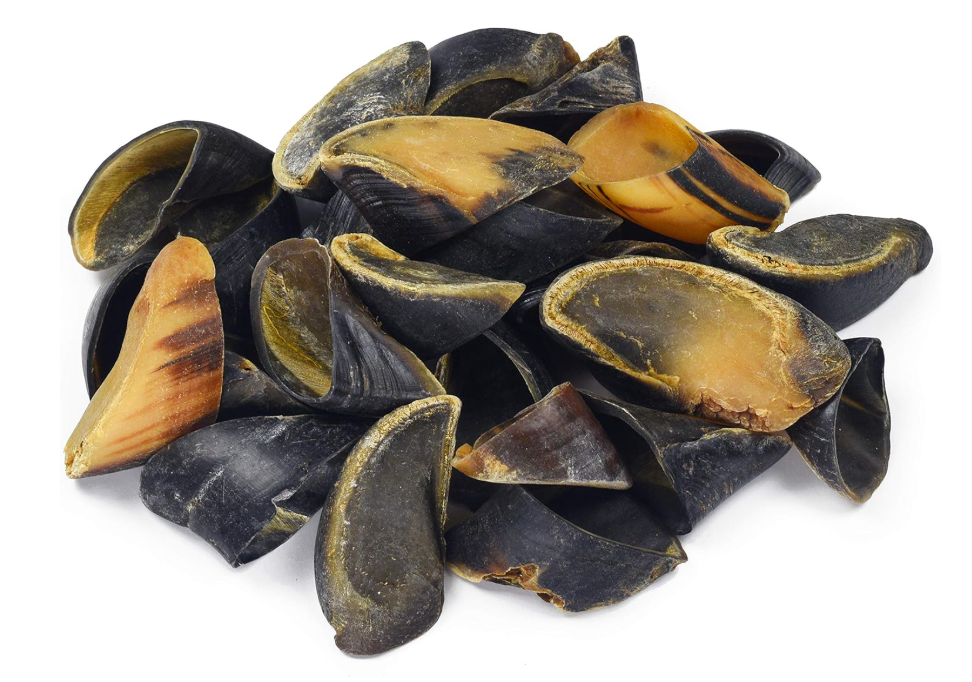 Pile of black and brown cow-hoof dog chews on a white background