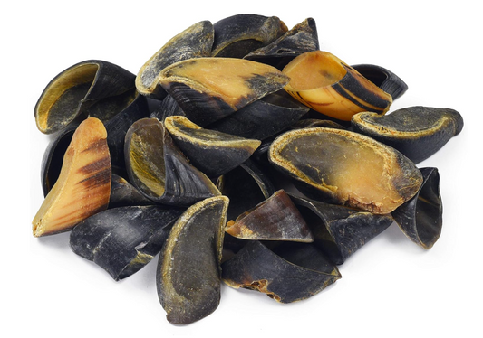 Pile of black and brown cow-hoof dog chews on a white background