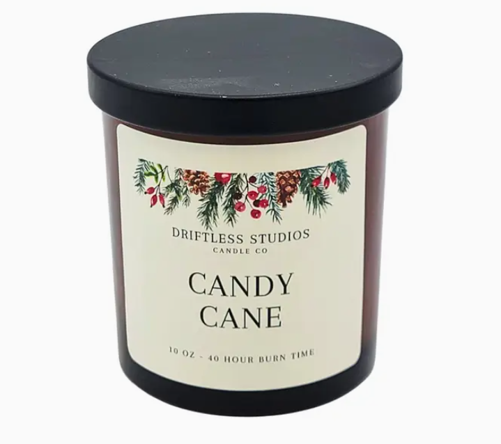 Candle with 'Driftless Studios Candle Co' label featuring Christmas-themed design on a white background