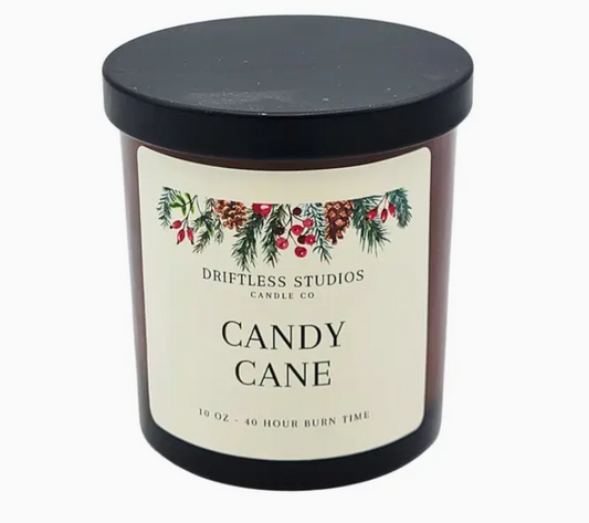 Candle with 'Driftless Studios Candle Co' label featuring Christmas-themed design on a white background