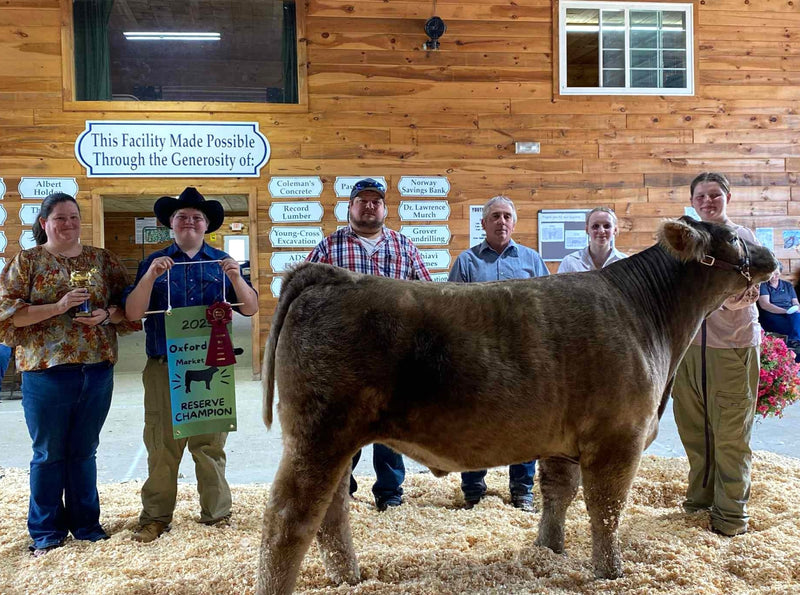Group of people with a cow in front of a wooden building with signs on the wall.
