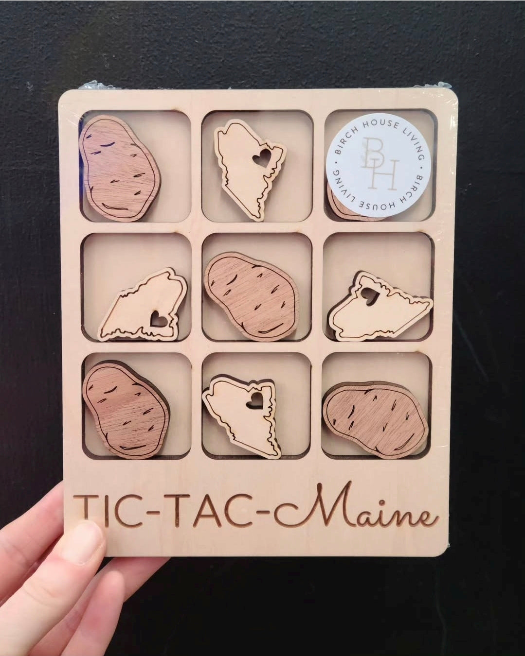 Tic-tac container with wooden shapes of Maine and potatoes on a black background