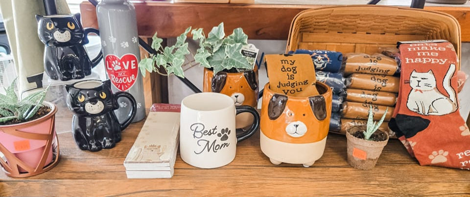 Display of various items including mugs, planters, and decorative boxes on a wooden shelf.