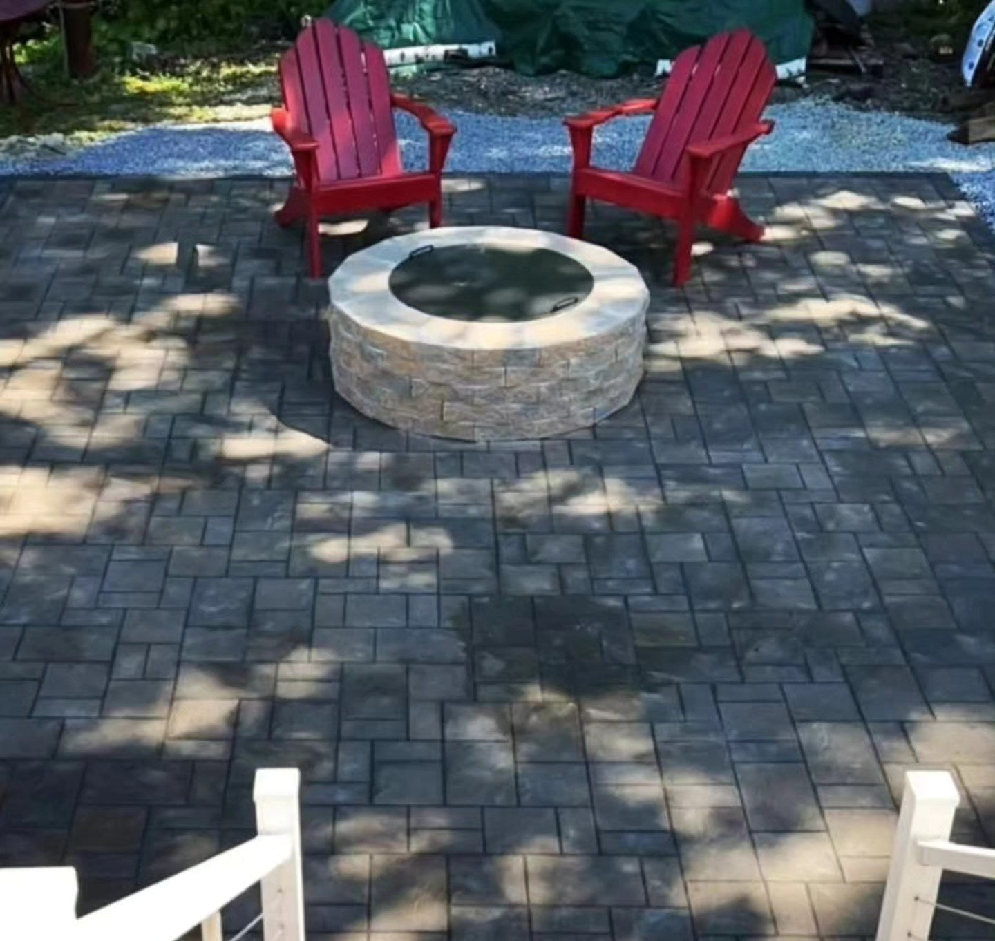 Two red Adirondack chairs around a stone fire pit on a patio.