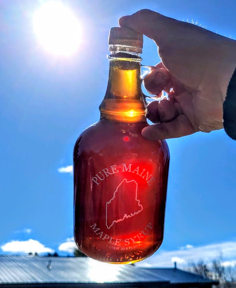 hand holding up a jar of maple syrup against a blue sky background.